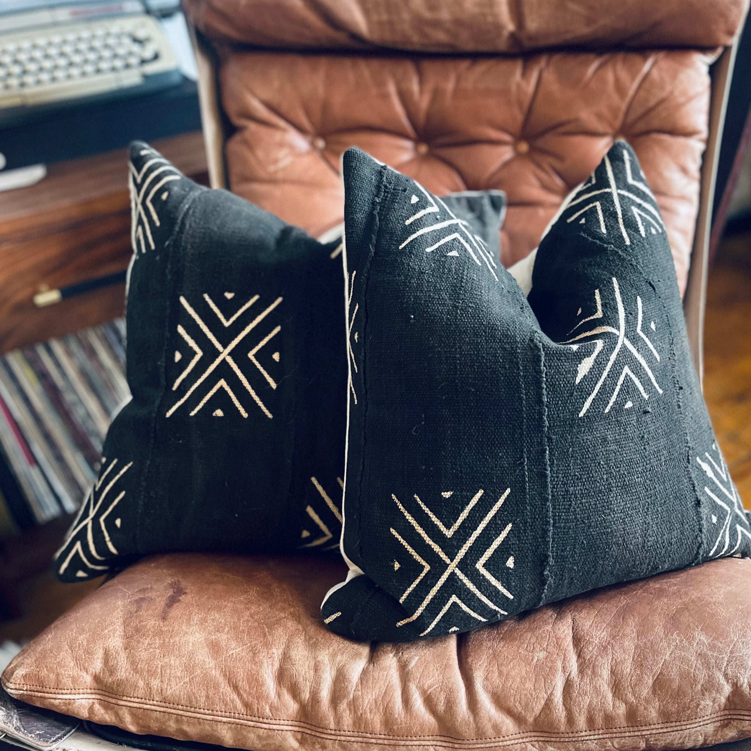 two black and white geometric textured pillows sitting on a brown leather chair in a masculine living room setting