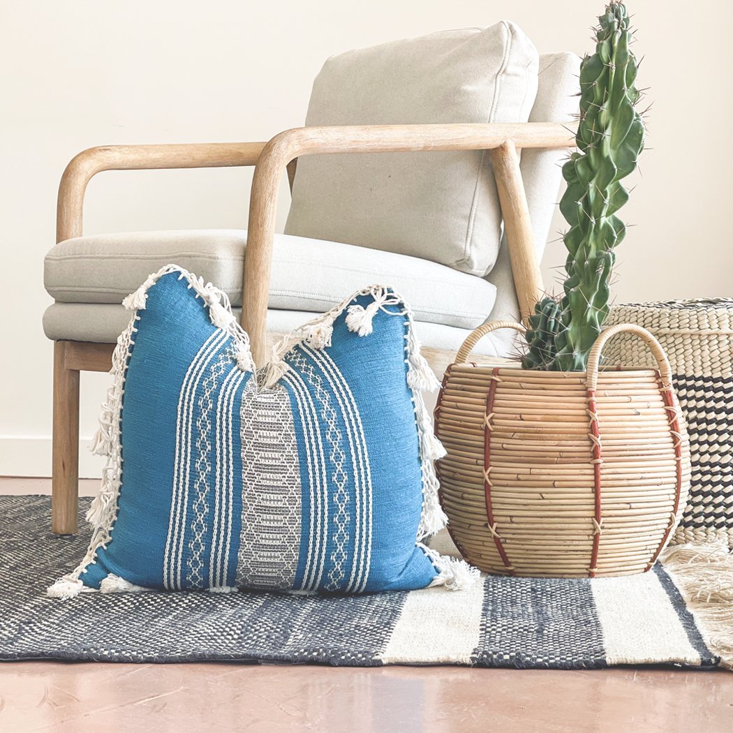 Colorful Throw Pillow With Fringe | Multiple Colors - BAJA CHICneed verificationNEWHUNTEDFOX - Turquoise and White hand - woven geometric pillow with textured details and fringe, styled on a light wood accent chair with a striped rug, wicker baskets, and a potted cactus for a modern bohemian vibe