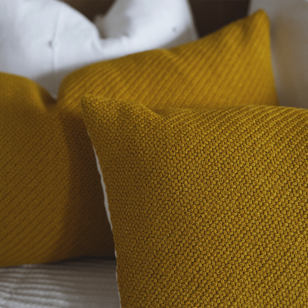 close-up of woven mustard yellow pillow on patterned fabric