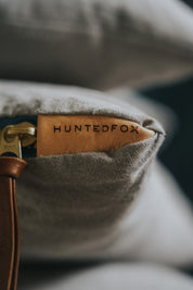 Stone Washed Light Grey Accent Pillow - CHIC CHALETEssentialGreyHUNTEDFOX - Close - up of a leather tag with 'Hunted Fox' branding on a product.