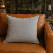 Stone Washed Light Grey Accent Pillow - CHIC CHALETEssentialGreyHUNTEDFOX - Gray pillow on a brown leather sofa in a cozy living room setting.