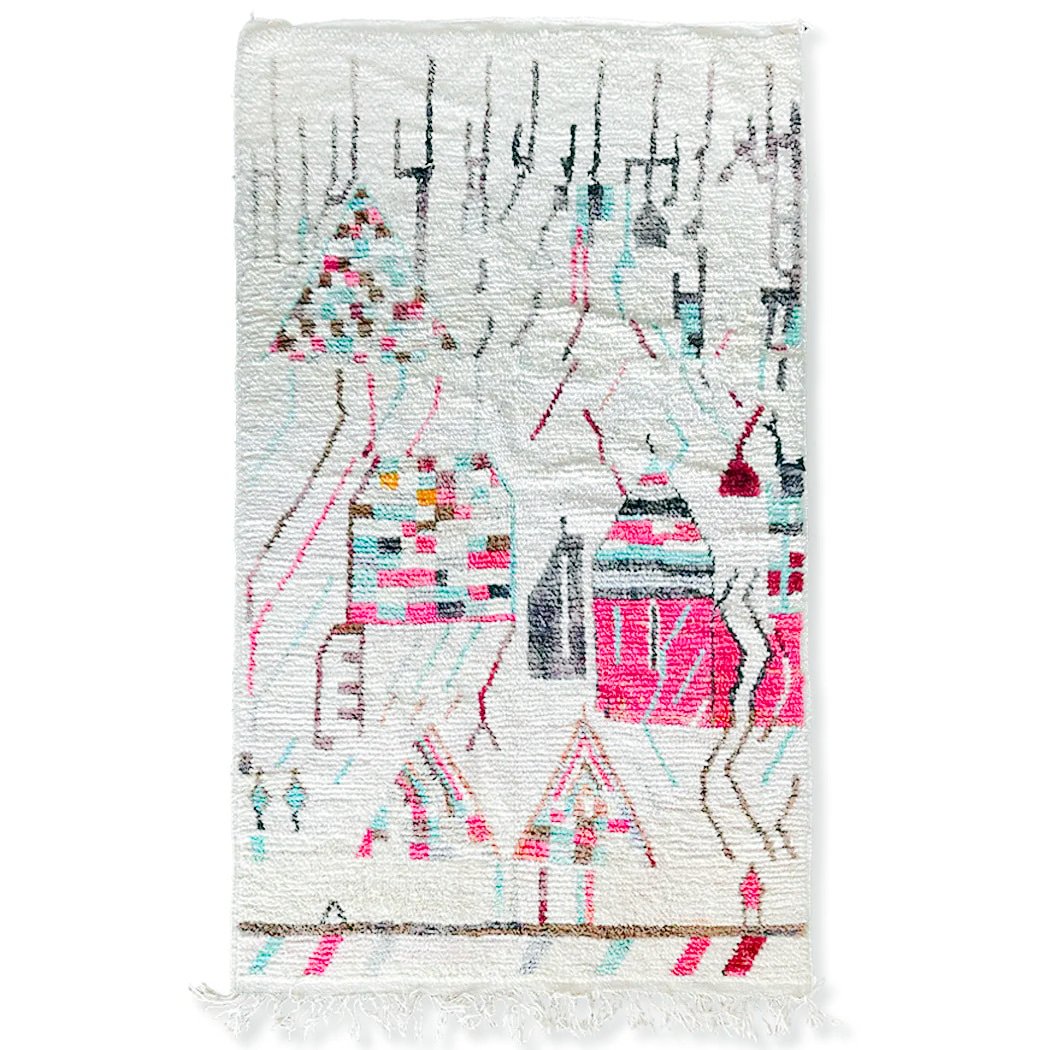 Handwoven Moroccan-style area rug with abstract village motifs in vibrant colors, including pink, turquoise, and black, on a cream background with fringe detailing.