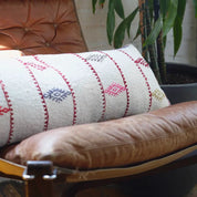 Handwoven cotton lumbar pillow with red and blue embroidery on an ivory base, styled on a leather armchair.