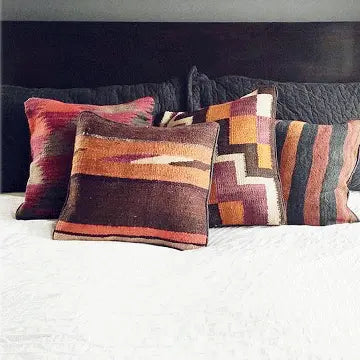 vintage kilim pillows piled on top of a bed with white comforter and black headboard