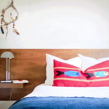 red pillow with fish on it sitting on top of a white bed with wood background and vintage indigo throw on bed