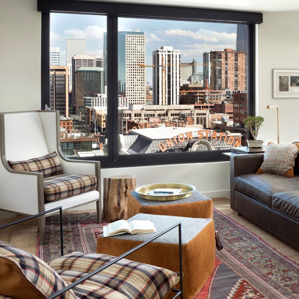 bachelor pad living room with plaid and suede custom ottomans and leather sofa overlooking Denver skyline