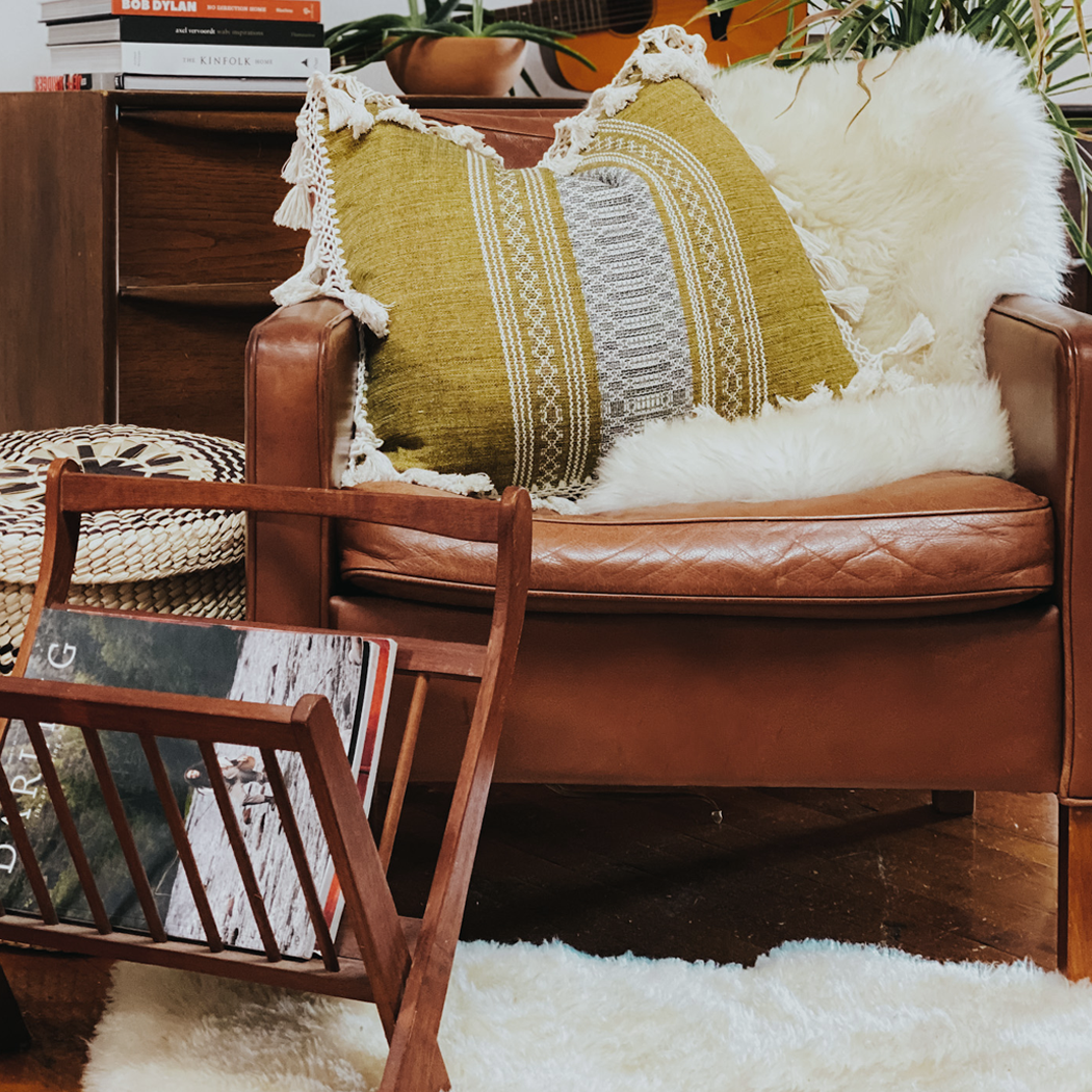 mustard yellow pillow with fringe sitting on a leather chair