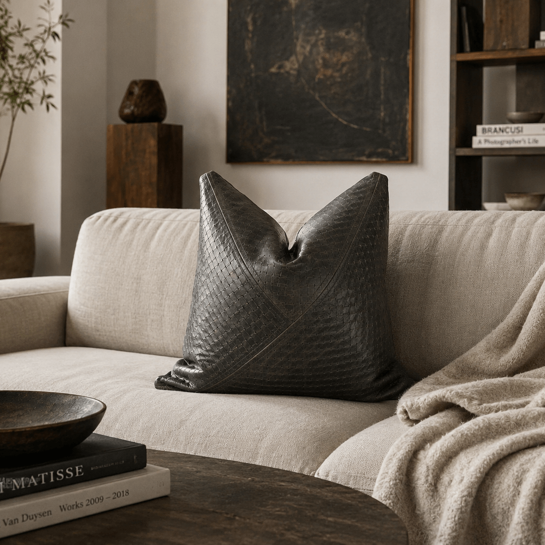 Charcoal Textured Leather Accent Pillow | Modern Elegance - BlackhunterLEATHERHUNTEDFOX - Gray textured pillow on a beige sofa with a bowl and books on a wooden table.