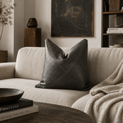 Charcoal Textured Leather Accent Pillow | Modern Elegance - BlackhunterLEATHERHUNTEDFOX - Gray textured pillow on a beige sofa with a bowl and books on a wooden table.