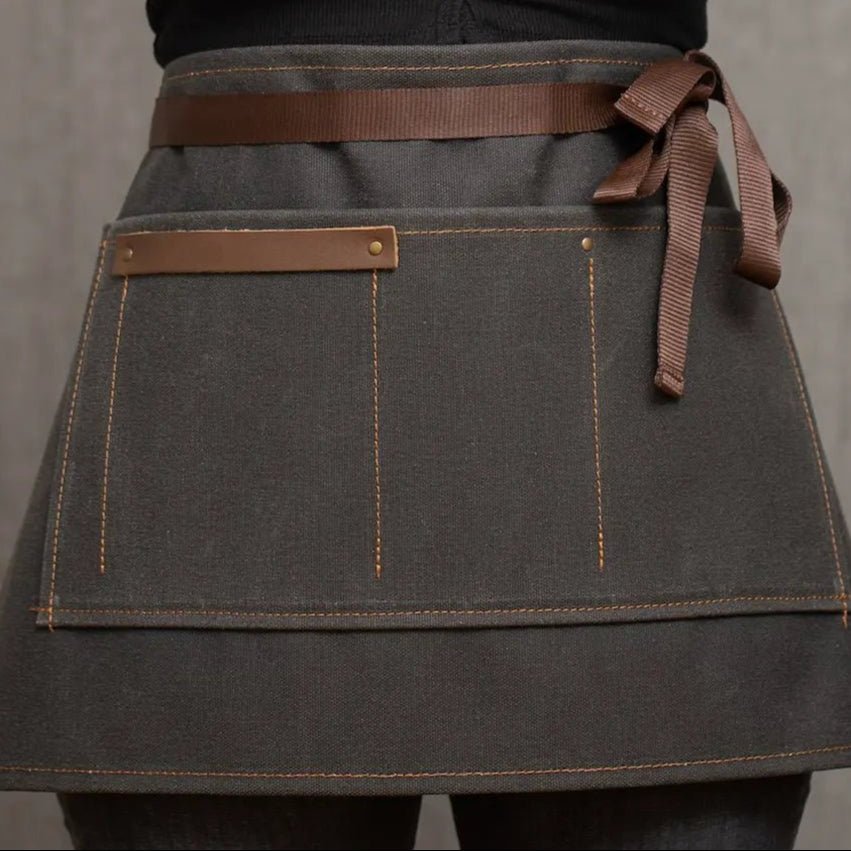 Custom Waxed Canvas Half Apron – Leather Trim Utility Belt for Baristas, Bartenders & Artists - H|F AtelierINDUSTRYneed verificationHUNTEDFOX - Handmade waxed canvas half apron with brown leather trim, worn by barista or bartender – custom utility apron by HUNTEDFOX