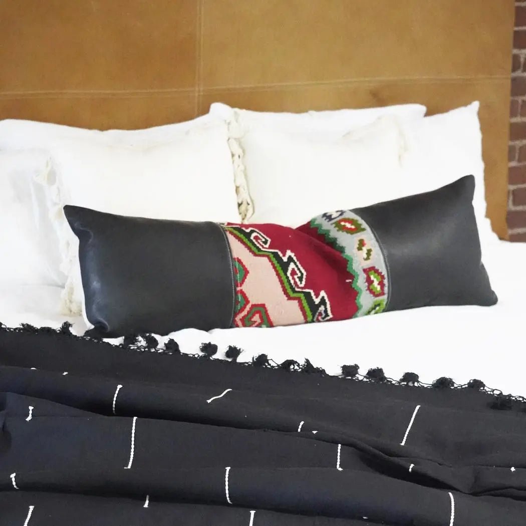 Handmade long lumbar pillow with black leather sides and vintage red and green kilim center on a white bed