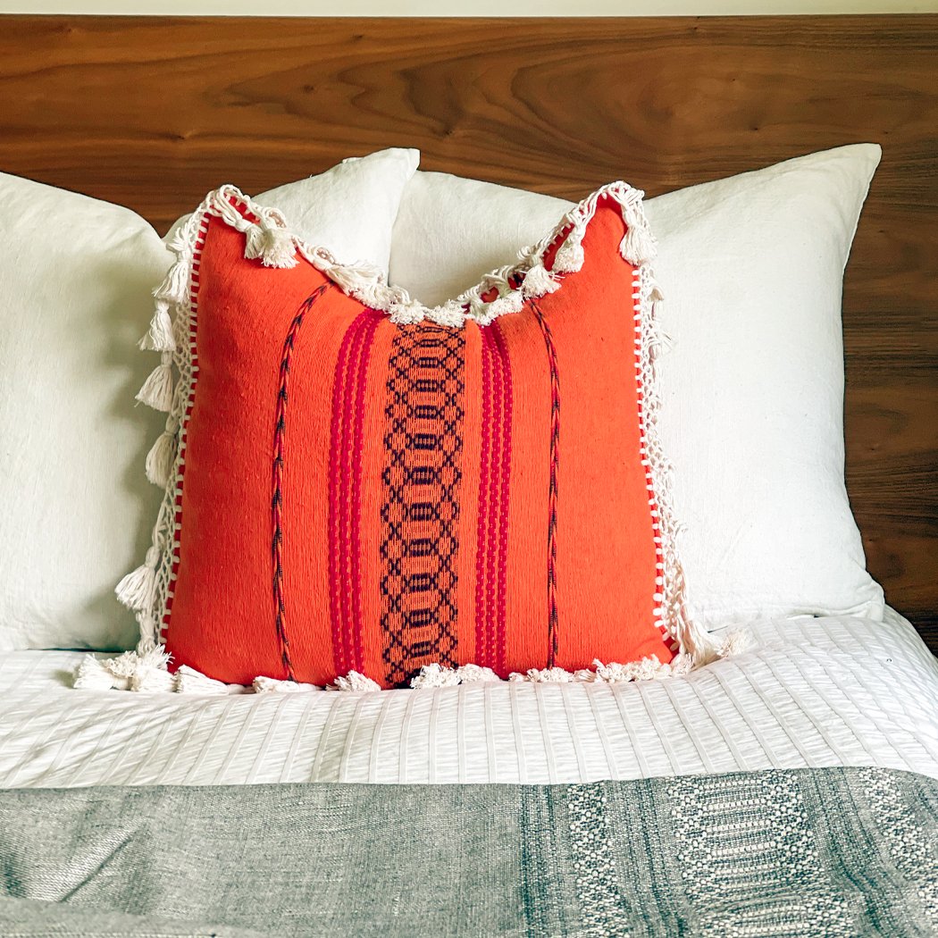 Orange Pillow With fringe sitting on a bed